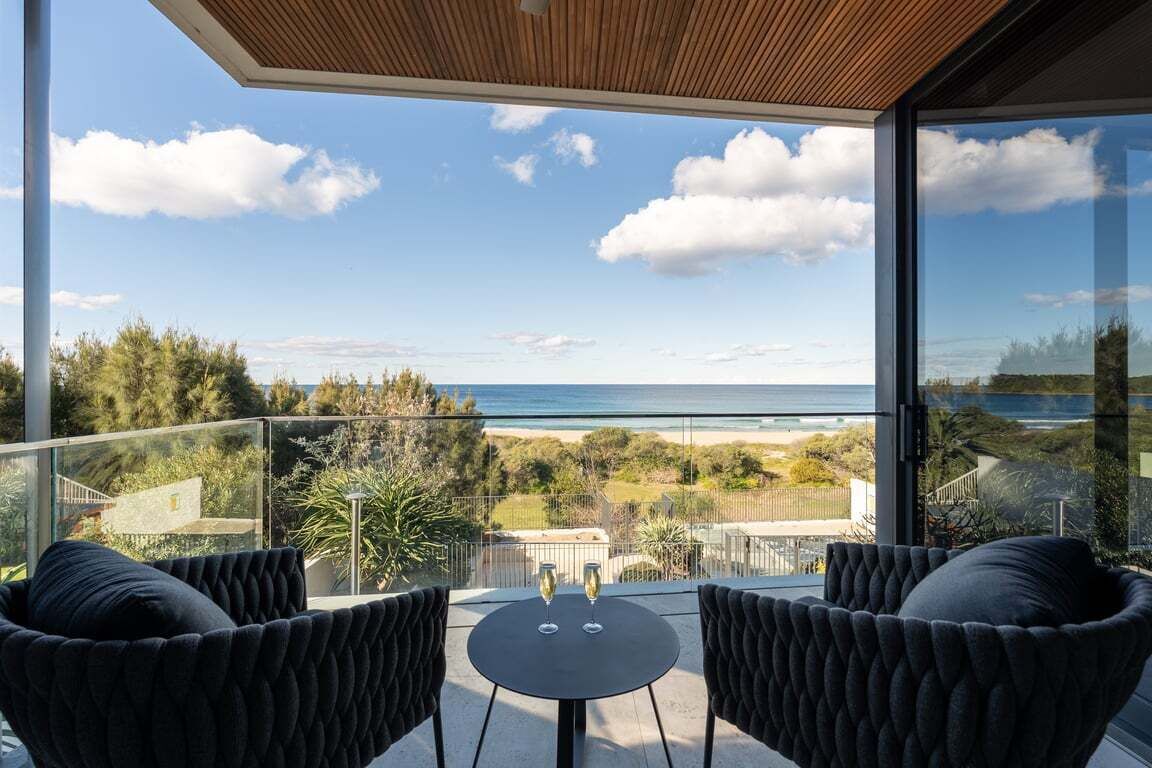 A balcony with a view of the sea, two chairs, and a table with glasses.