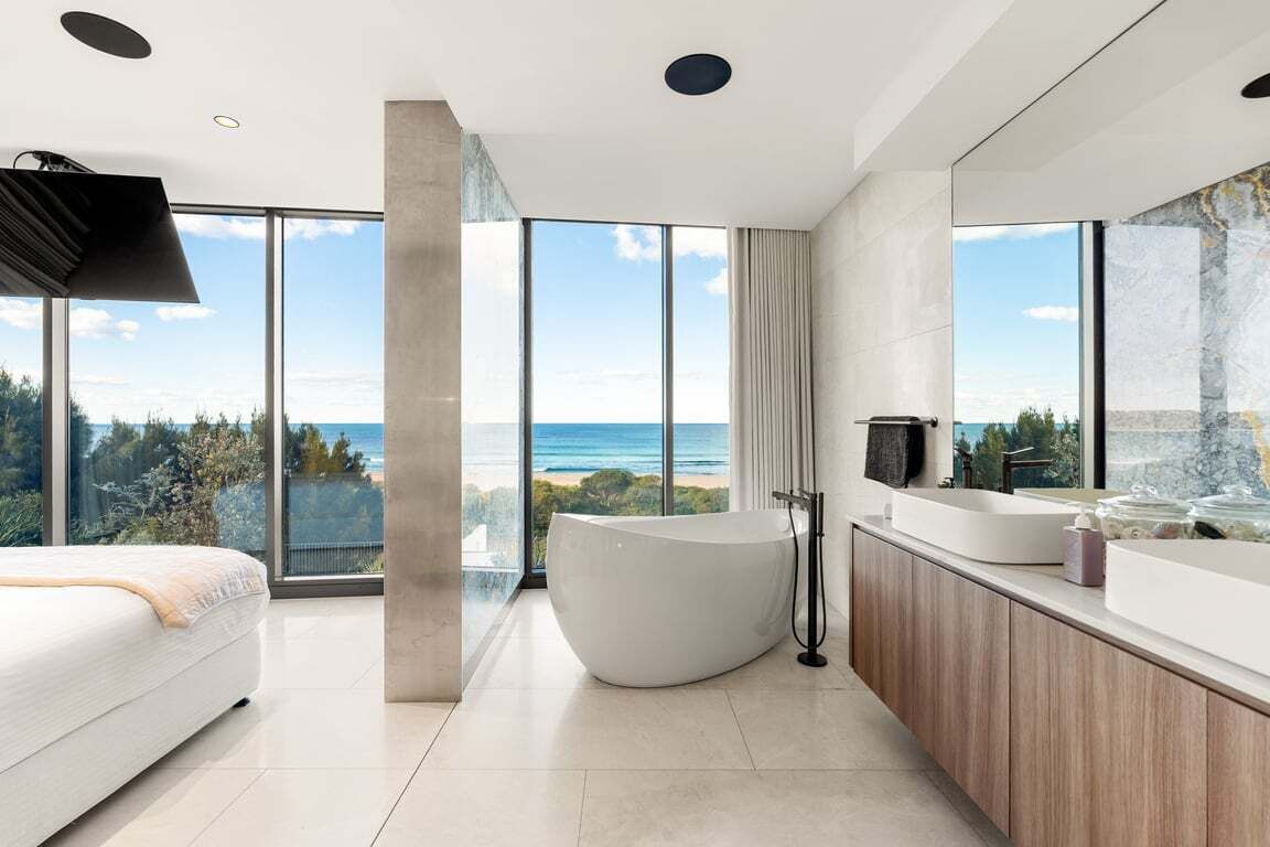 A modern bathroom with a large bathtub, a vanity with a mirror, and a view of the ocean.