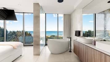 A modern bathroom with a large bathtub, a vanity with a mirror, and a view of the ocean.