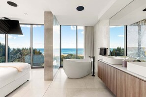 A modern bathroom with a large bathtub, a vanity with a mirror, and a view of the ocean.