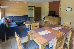 Ein Wohnzimmer mit einer Couch, einem Couchtisch, einem Esstisch mit Stühlen, einem Fernseher und einer Uhr an der Wand.