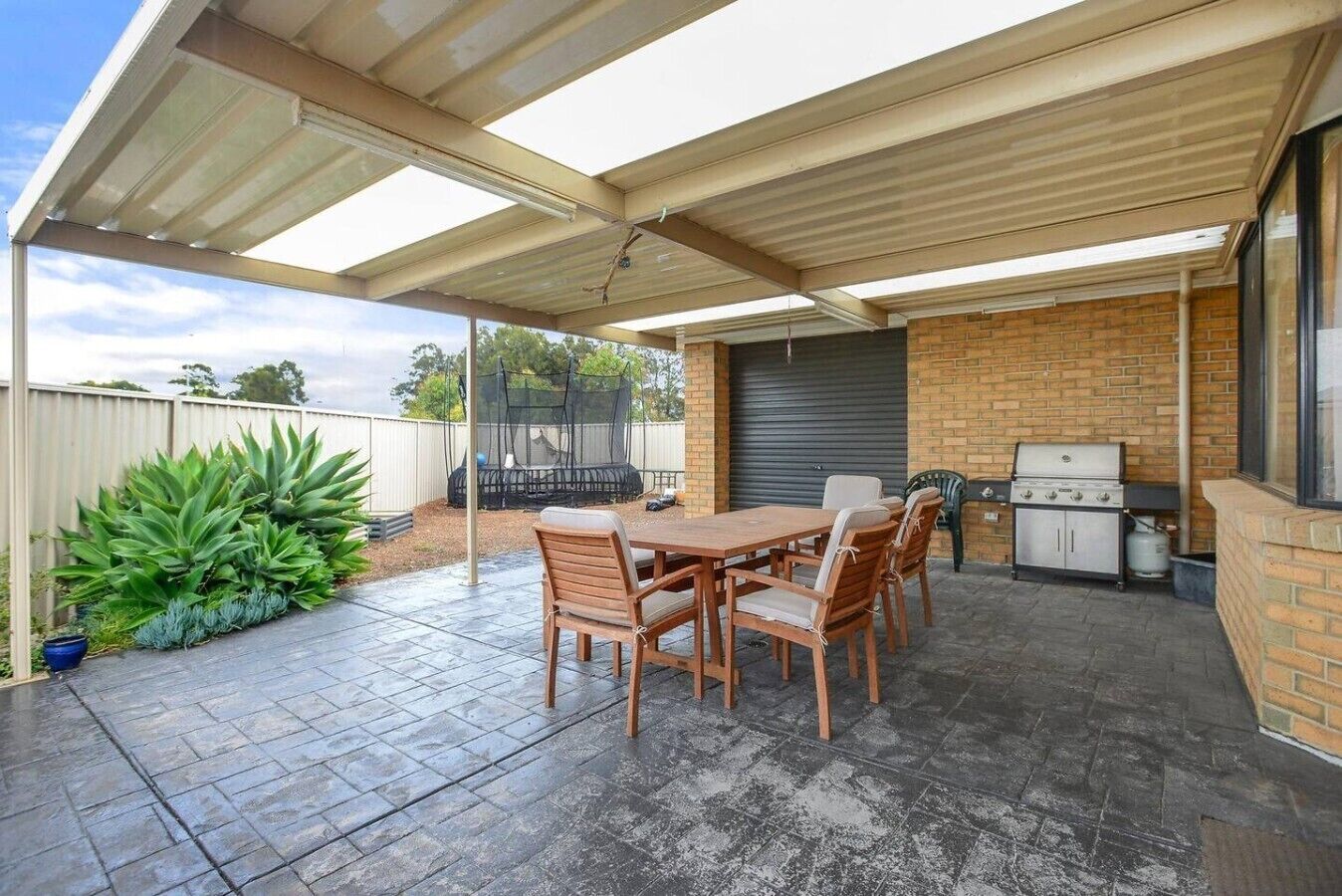 A covered patio with a table and chairs, a grill, and a trampoline.