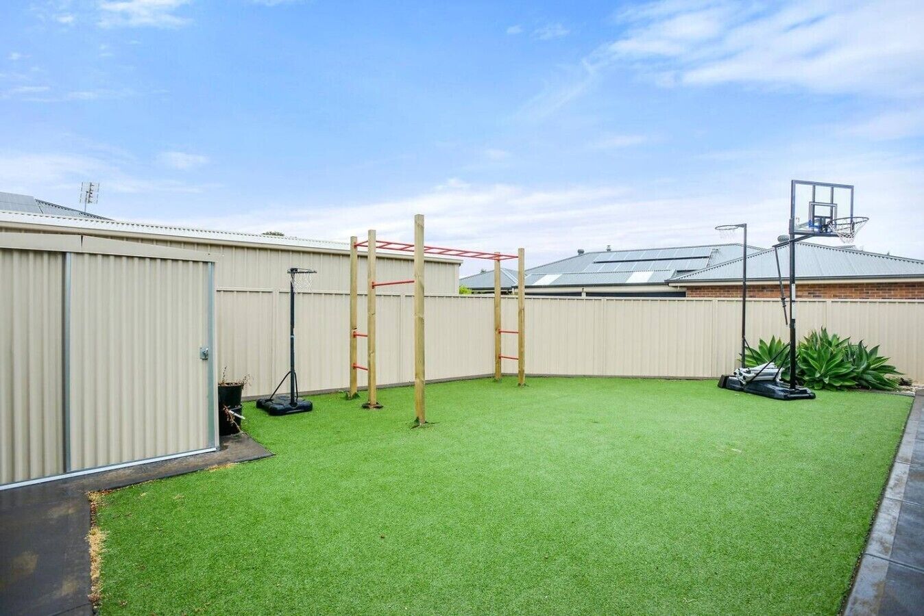 A backyard with artificial grass, a basketball hoop, a climbing structure, and a shed.