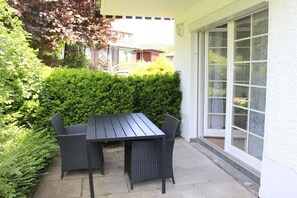 An outdoor patio with a table and chairs, surrounded by greenery and a white building facade. - Holiday apartment with 2 bedrooms (Braunlage)