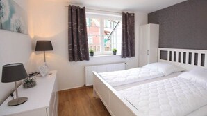 Ein Schlafzimmer mit zwei Betten, einem Schreibtisch mit Lampe, einem Heizkörper und einem Fenster mit Vorhängen.