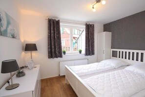 A bedroom with two beds, a desk with a lamp, a radiator, and a window with curtains. - Holiday apartment with 2 bedrooms (Braunlage)