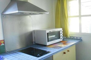A kitchenette with a built-in oven, a stovetop, and a window with yellow curtains. - Maffone la laupie gîte COCO (La Laupie)