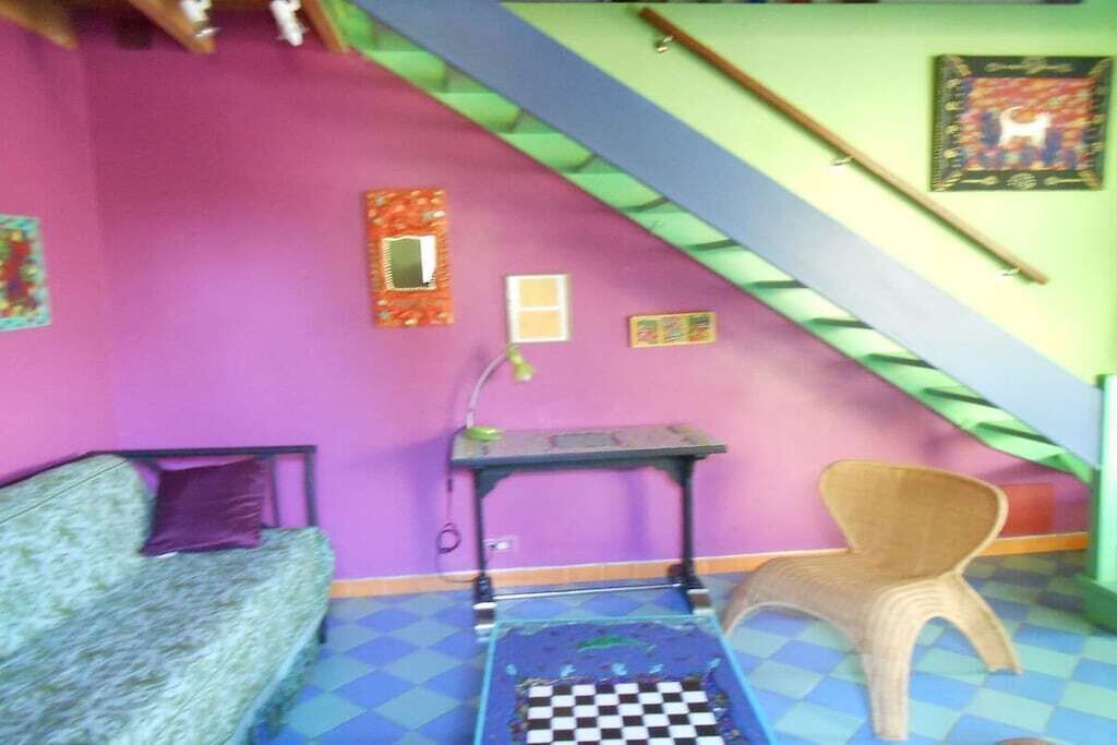 Ein Zimmer mit lila Wand, kariertem Boden, einem Bett, einem kleinen Tisch, einem Stuhl und einer Treppe.