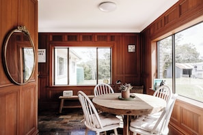 A dining area with a round wooden table, white chairs, and a large window with a view of the outdoors. - Mid North Coast Accomodation and Horsestay (Rawdon Island)