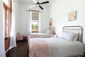 A bedroom with two beds, a ceiling fan, a window with curtains, a bedside table, and a wall-mounted painting. - Mid North Coast Accomodation and Horsestay (Rawdon Island)