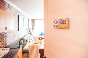 A hotel room with a wooden door, a sign indicating room services, a kitchen area with a marble countertop, and a seating area with a sofa and a table. - F305 2-bedroom apartment in lovely with Playground and Kidclub near Beach (Nongkae)