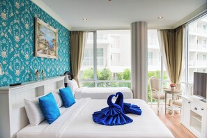 A hotel room with two beds, a painting on the wall, a desk with a chair, and a view of buildings through the window. - F305 2-bedroom apartment in lovely with Playground and Kidclub near Beach (Nongkae)