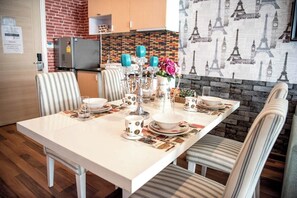 A dining area with a white table set for four, striped chairs, a brick wall, and a mural of the Eiffel Tower. - F305 2-bedroom apartment in lovely with Playground and Kidclub near Beach (Nongkae)