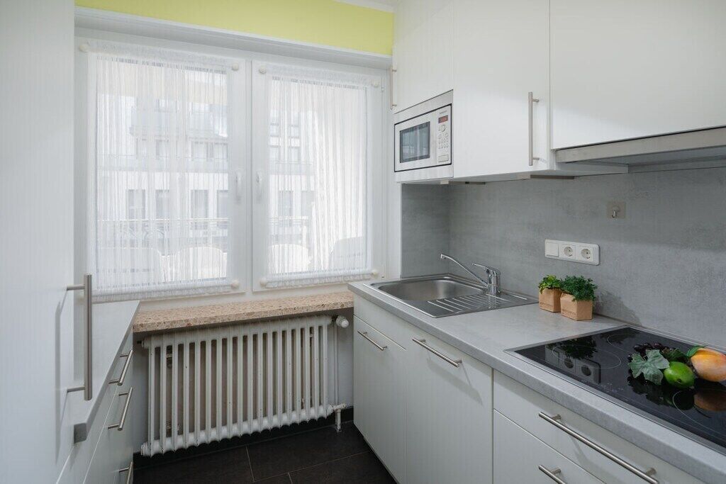 Eine Küche mit Fenster, einer Mikrowelle, einem Spülbecken und einer Arbeitsplatte mit Pflanzen.