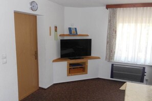 A room with a television on a wooden stand, a door, a radiator, and a window with curtains.