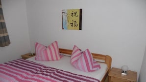 Uma cama de solteiro com manta listrada, duas almofadas, mesa de cabeceira com luminária e uma obra de arte na parede.