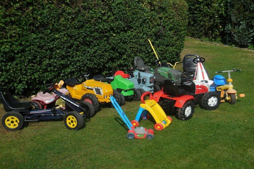 A collection of toy tractors and lawn mowers on a grassy lawn.