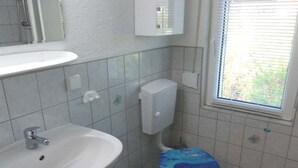 Casa de banho com lavatório branco, sanita com assento azul e janela com persianas.