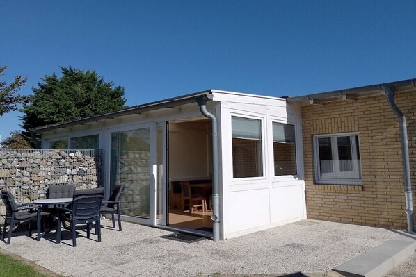 Een modern huis met een patio, voorzien van een tafel, stoelen, een stenen muur en een ruimte met glazen wanden.