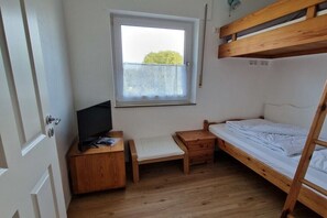 Een kleine kamer met een stapelbed, een bureau met een televisie, een raam met uitzicht en een deur.