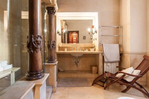 Un baño con un espejo grande, una silla de madera y un perchero para toallas.