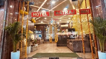 L’entrée d’un hôtel, avec un comptoir d’accueil, un escalier menant au hall et une enseigne indiquant « Natraj Inn ».