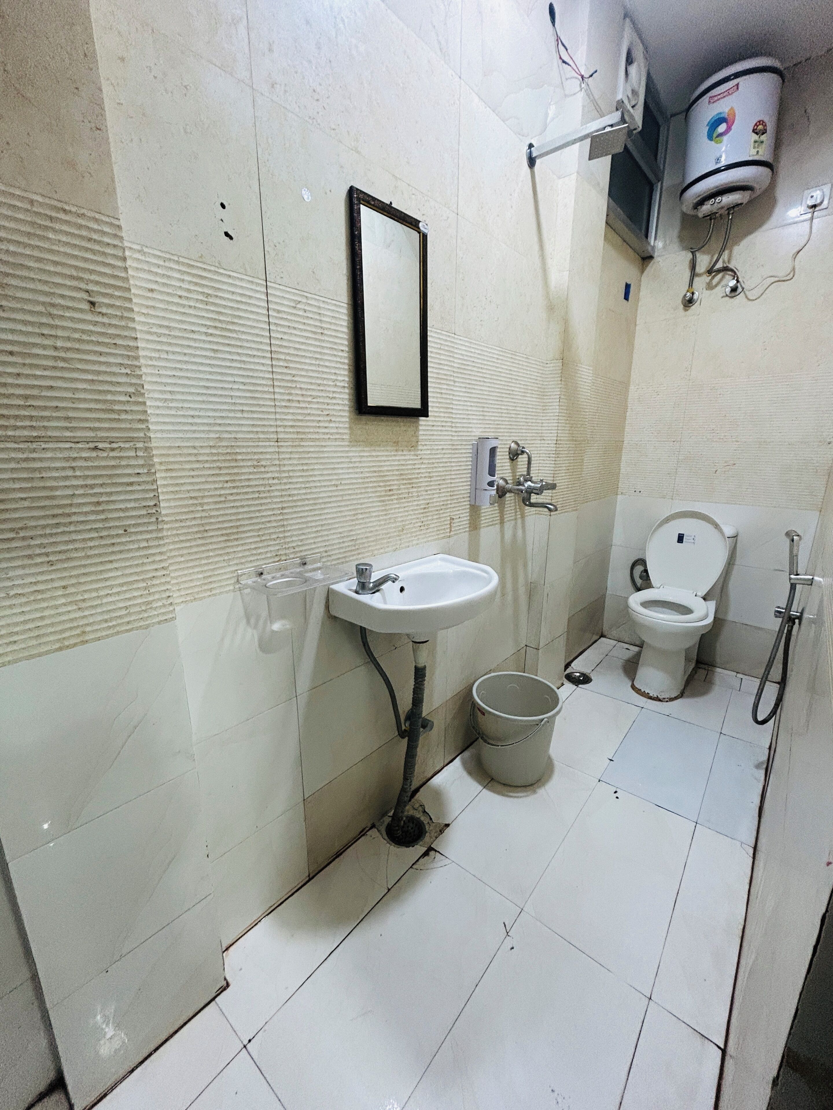 Une salle de bain équipée d’un lavabo, d’un miroir, de toilettes et d’un seau.