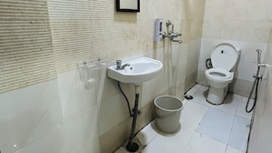A bathroom with a sink, mirror, toilet, and a bucket. - HOTE NATRAJ INN  (Varanasi)