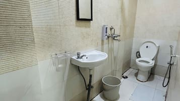 Une salle de bain équipée d’un lavabo, d’un miroir, de toilettes et d’un seau.