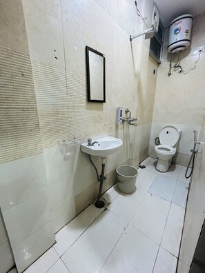 A bathroom with a sink, mirror, toilet, and a bucket. - HOTE NATRAJ INN  (Varanasi)