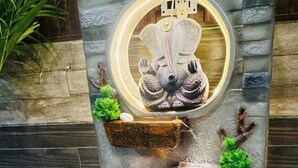 Una fuente de piedra con una estatua, tres macetas con plantas y un foco circular.