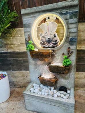 Una fuente de piedra con una estatua, tres macetas con plantas y un foco circular.
