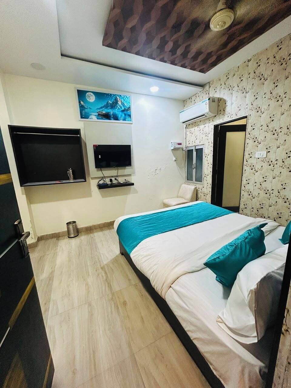 A hotel room with a bed, a television, a wall-mounted air conditioner, and a small window.