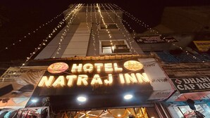 Exterior del Hotel Natraj Inn con un letrero llamativo, una entrada visible y luces colgantes.