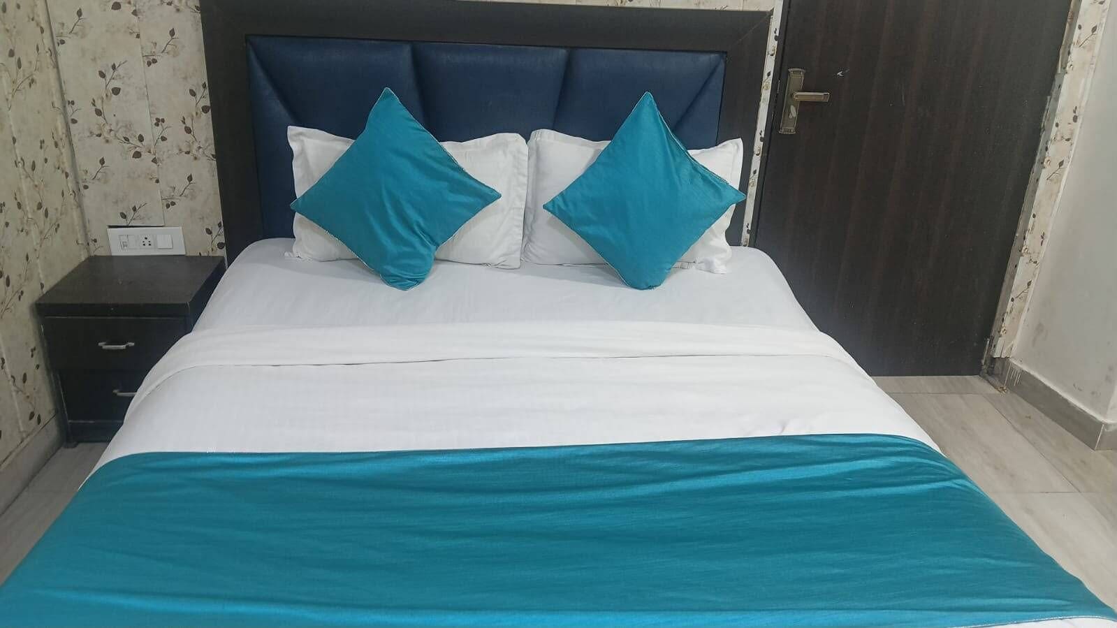 A bed with a white and teal bedspread, two teal pillows, and a dark headboard.