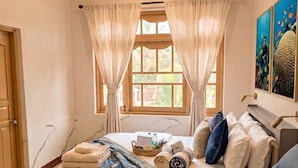 Habitación de hotel con cama, sofá, ventana con cortinas, equipo de aire acondicionado y obra de arte en la pared.