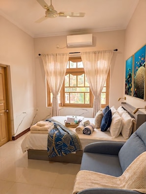 A hotel room with a bed, a sofa, a window with curtains, an air conditioning unit, and artwork on the wall. - Ocean Stay & Dive (Fenfushi)