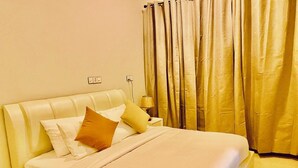 Una habitación de hotel con una cama, almohadas, una mesita de noche, una lámpara y cortinas.