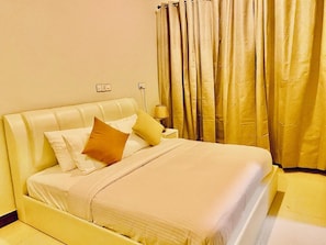 A hotel room with a bed, pillows, a nightstand, a lamp, and curtains. - Ocean Stay & Dive (Fenfushi)