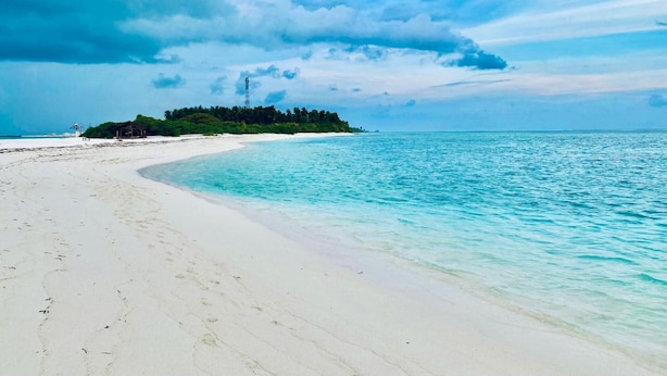 Una playa de arena blanca, agua turquesa cristalina y una pequeña isla con vegetación.