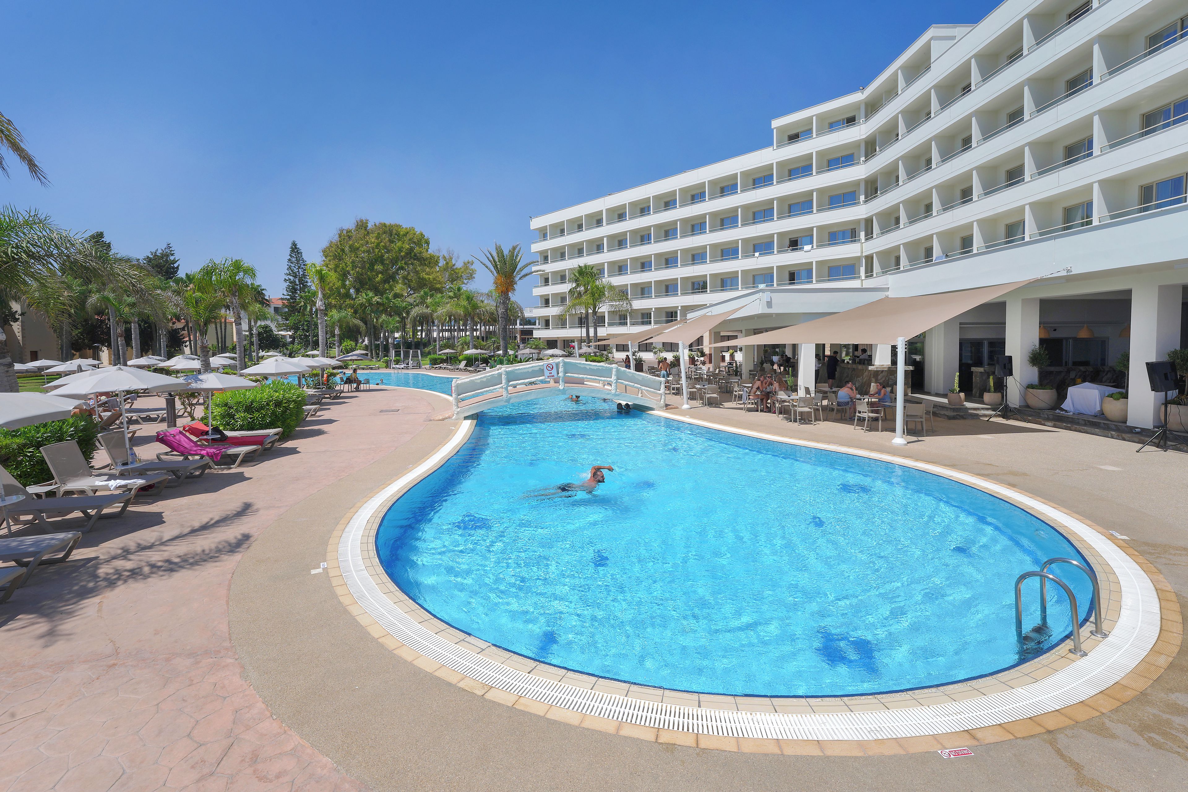 A hotel pool area with lounge chairs, a swimming pool, and a multi-story building in the background.
