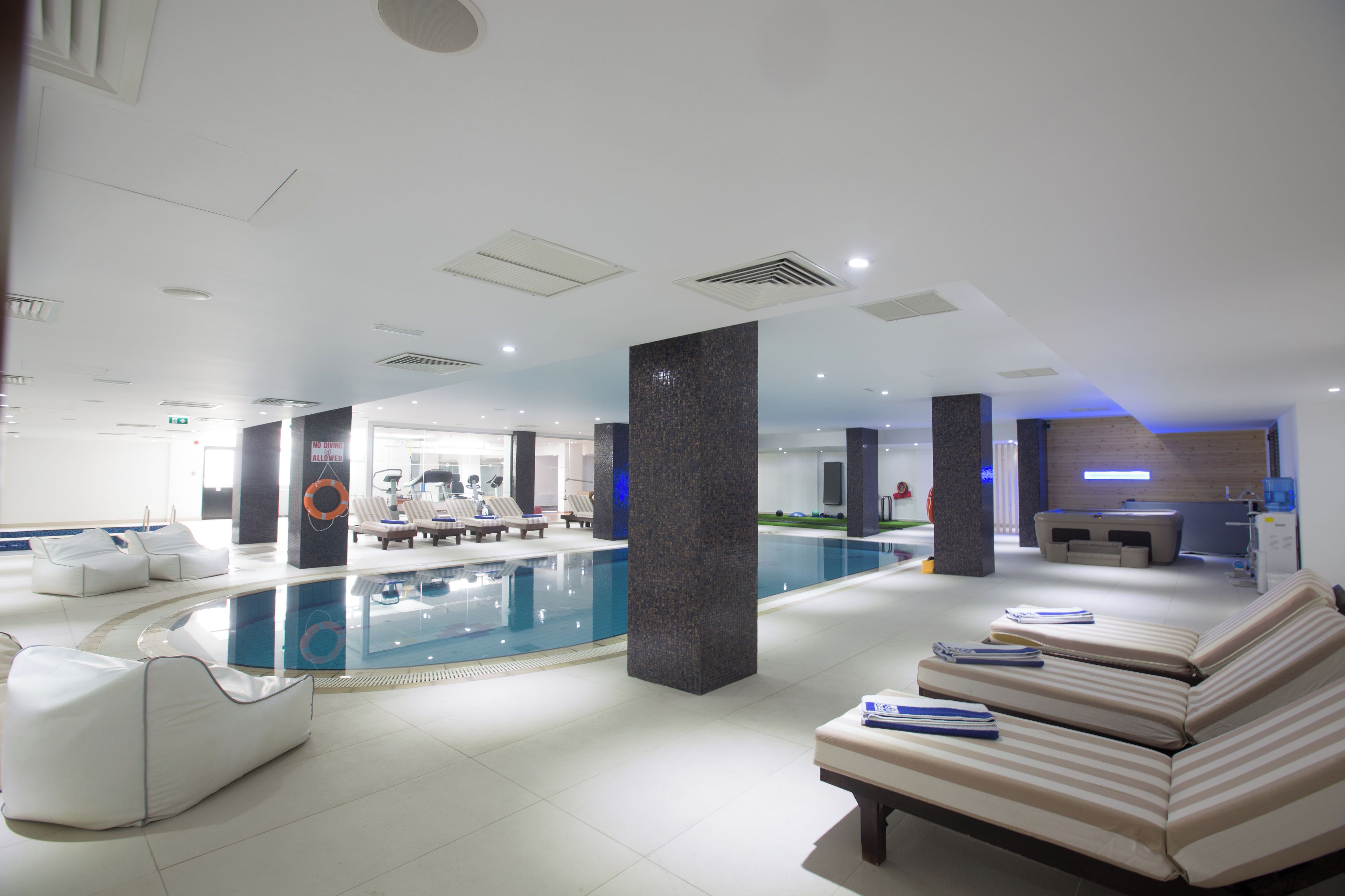 Un área de piscina interior moderna con sillones de descanso y un mostrador de recepción.