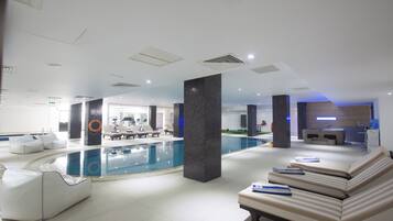 Un área de piscina interior moderna con sillones de descanso y un mostrador de recepción.
