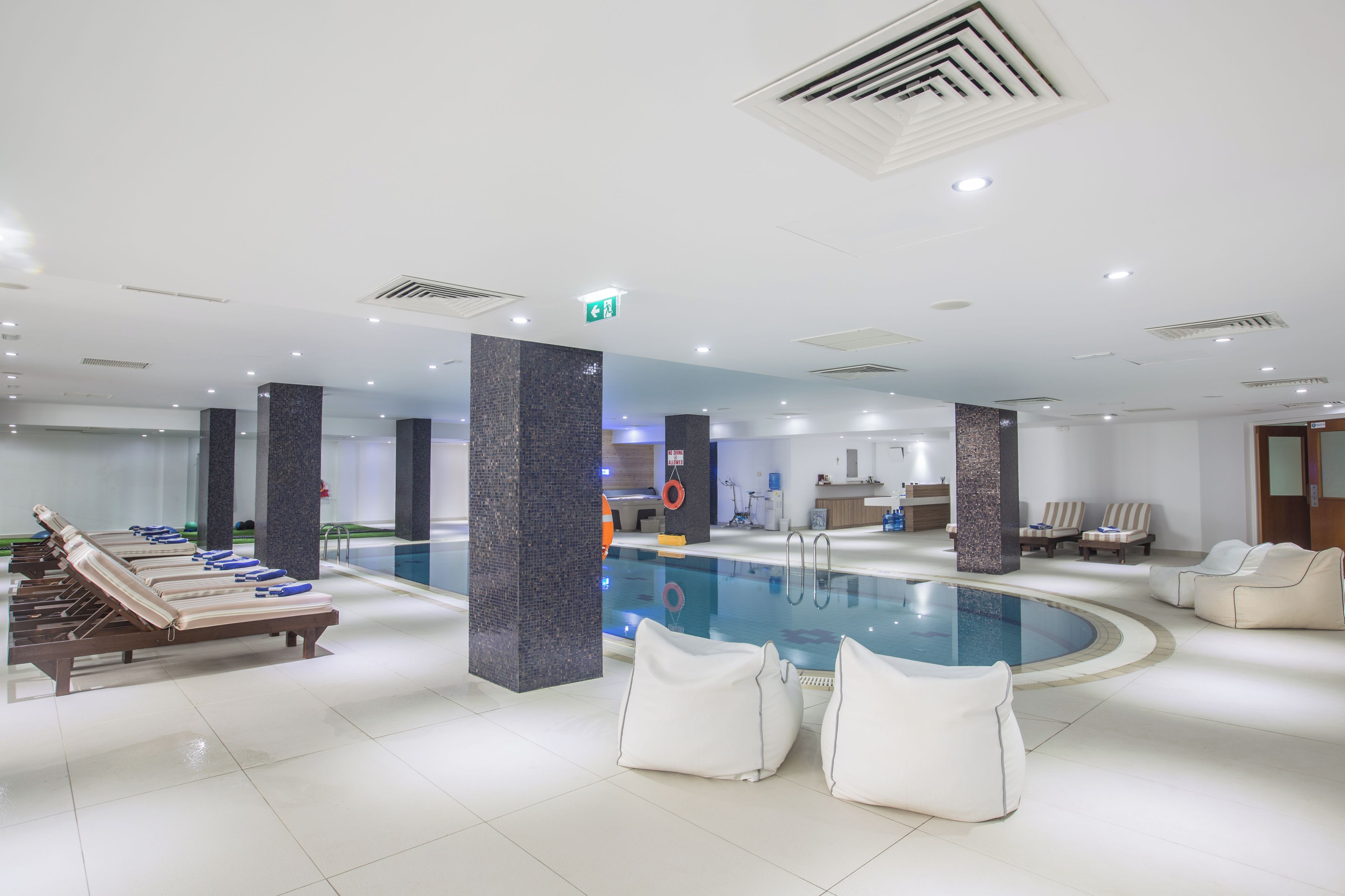 Uma área de piscina coberta moderna, com espreguiçadeiras, piscina e um balcão de recepção.