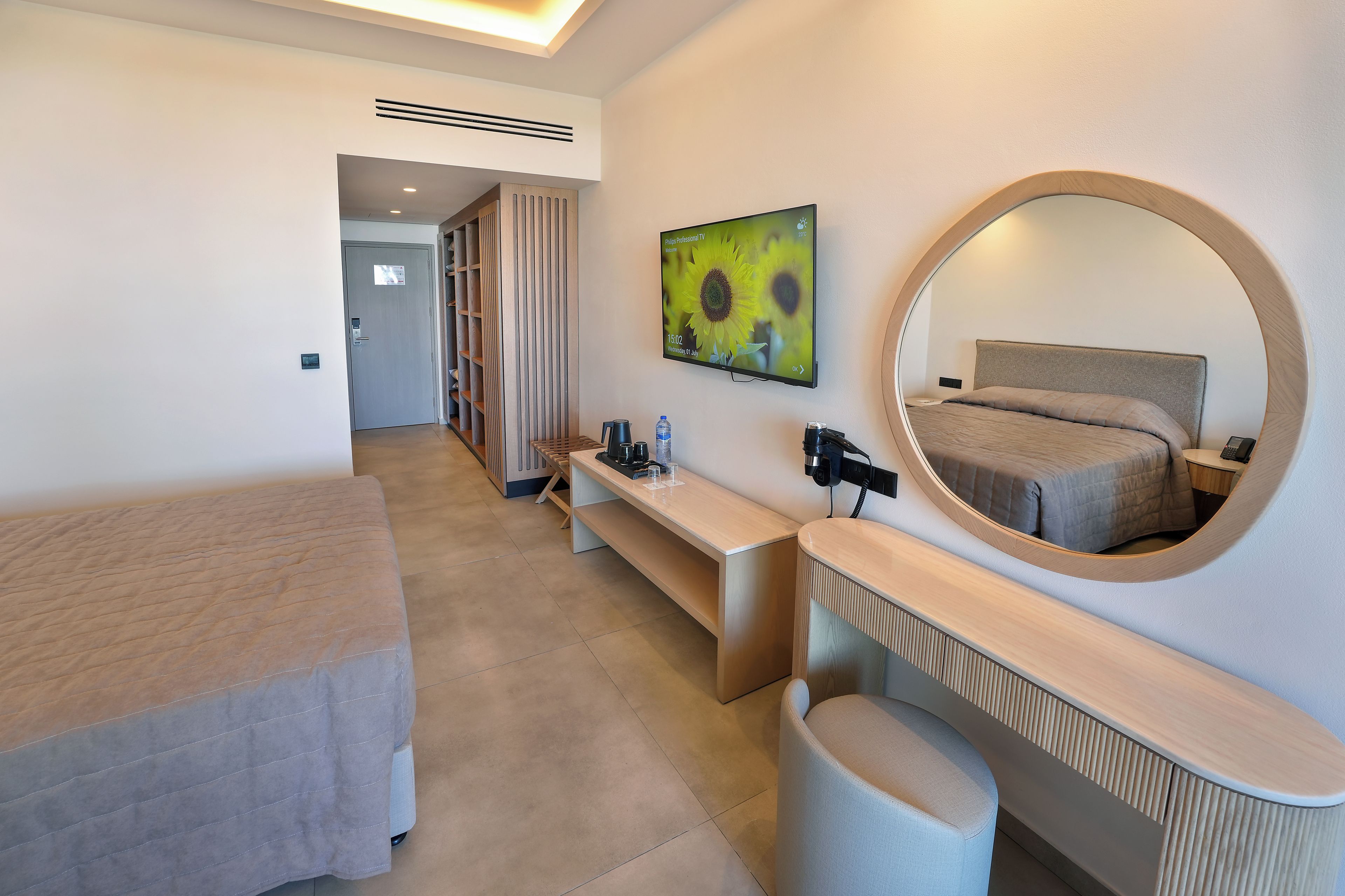 A modern hotel room with a bed, a desk, a chair, a mirror, and a TV.