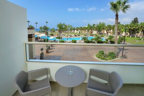 Un balcón con dos sillas y una mesa, con vistas a una zona de piscina con varias piscinas y palmeras.