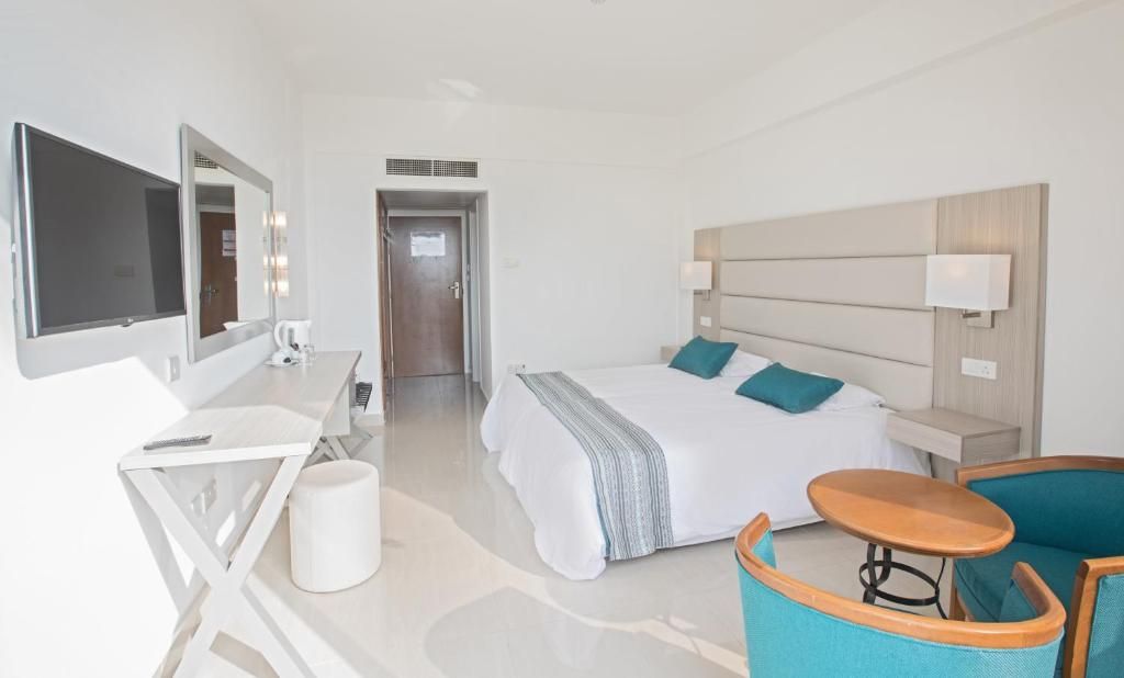 Une chambre d’hôtel avec un lit, un bureau, une chaise, une télévision et une porte.