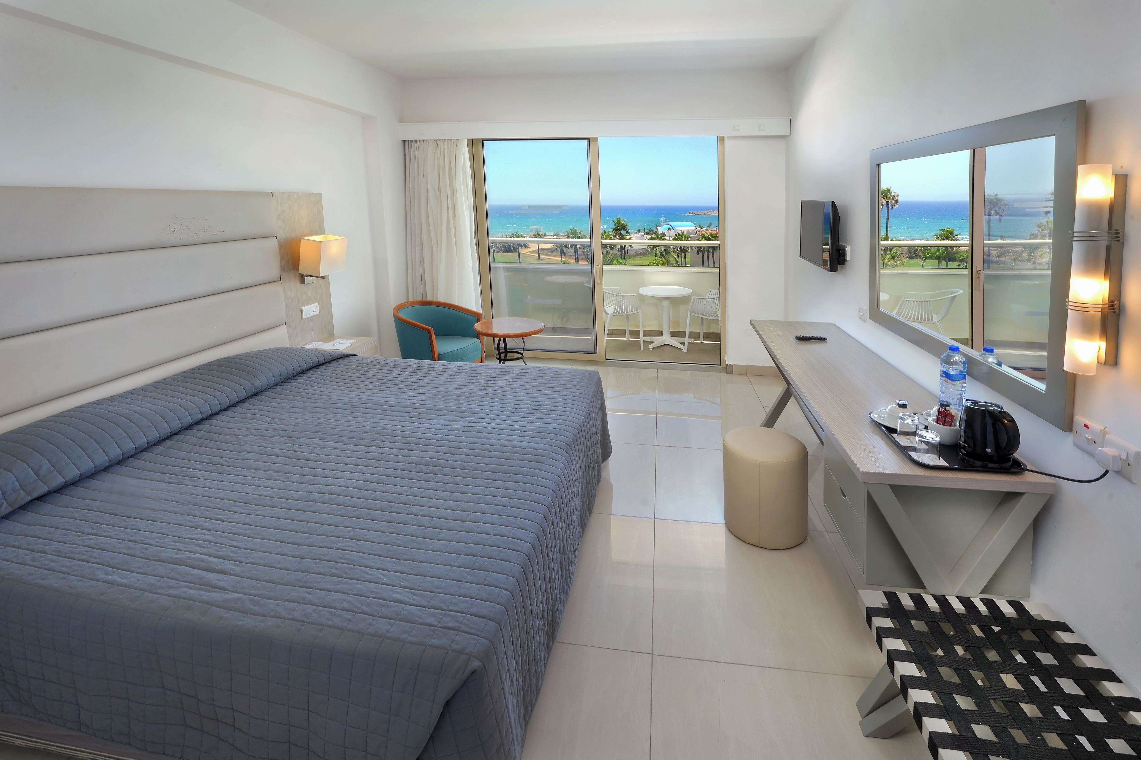 Habitación de hotel con cama, escritorio con silla, mesita, televisor y vista al océano.