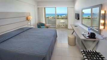 Habitación de hotel con cama, escritorio con silla, mesita, televisor y vista al océano.