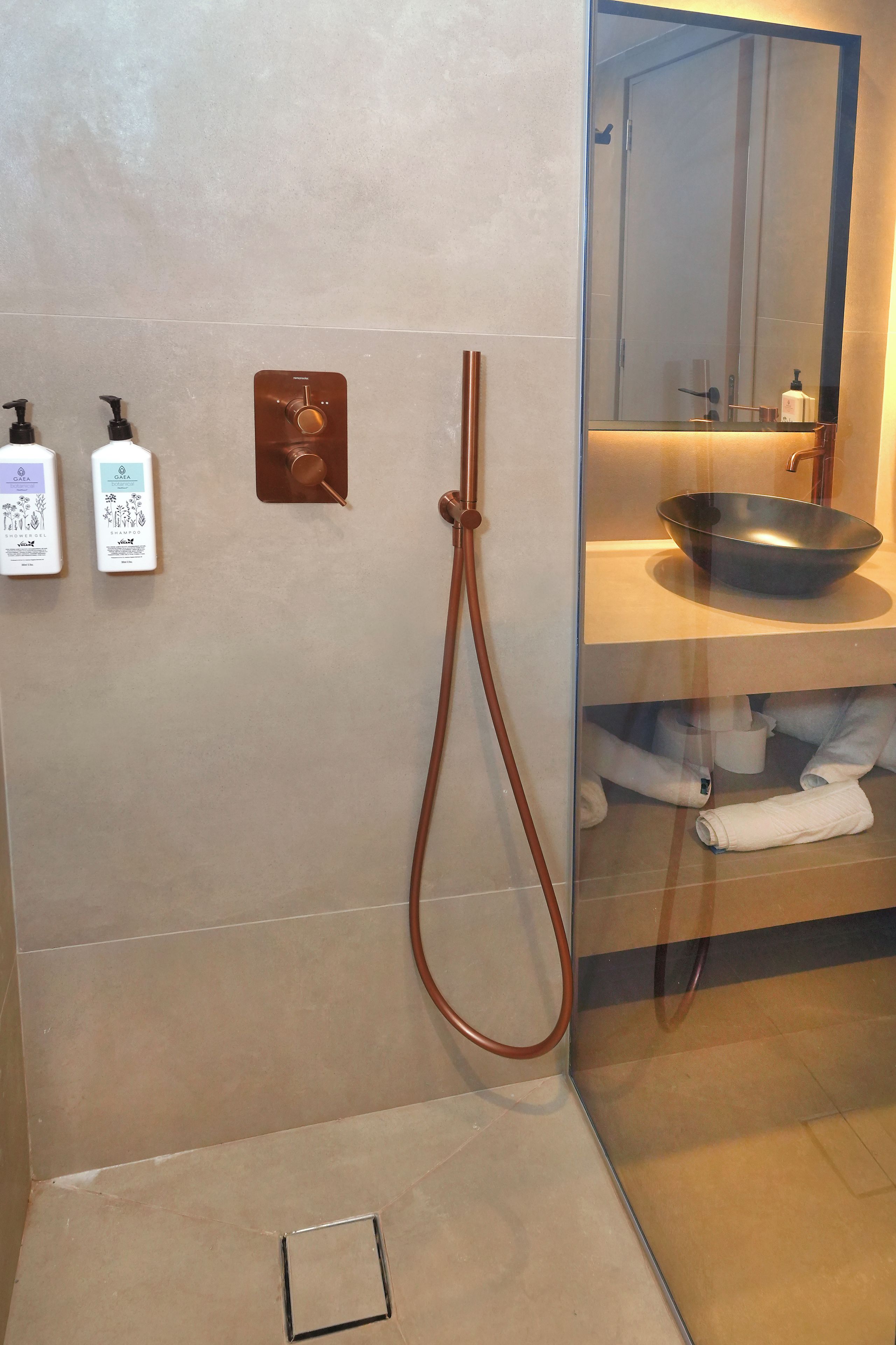Ein modernes Badezimmer mit Dusche, Waschbecken und Spiegel. An der Wand befinden sich zwei Shampooflaschen und eine Duschgelflasche.